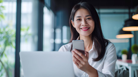 Senior middle aged Asian businesswoman manager ceo using smartphone and laptop in office working onlineの素材