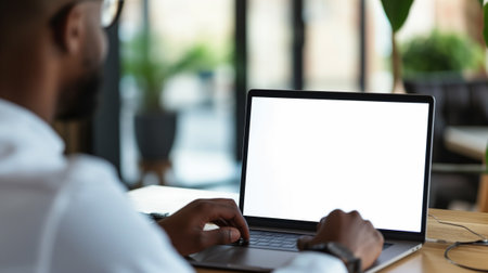 Over shoulder shot of a young man using computer laptop in front of an blank white computer screen in homeの素材