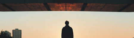 A contemplative silhouette of person standing bridge sunset with city buildings backgroundの素材