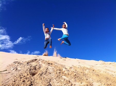 Girls jumping for joy off a sand dune. Clear bright blue skies in the background.の素材