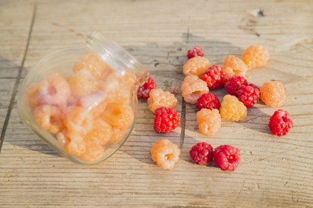 Red and yellow raspberries in a glass jar on a old wooden background