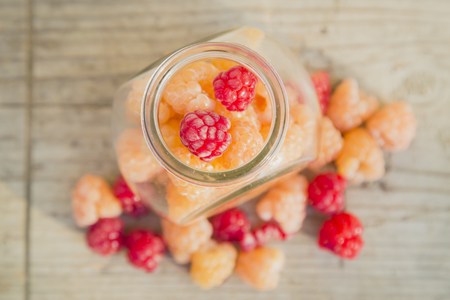 Red and yellow raspberries in a glass jar on a old wooden backgroundの写真素材