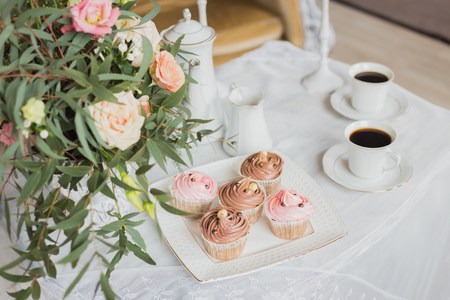 Wedding decorations zone - white table with bouquet, pink candles, cup of coffee and cupcakesの写真素材