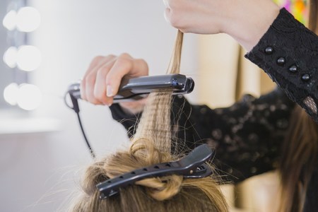 Close up of stylist hands with styling iron straightening woman hair at salonの写真素材