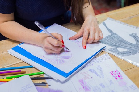 Close up shot - hands of professional tailor, designer drawing fashion sketch at atelier, studio. Dressmaking, creativity and tailoring conceptの写真素材