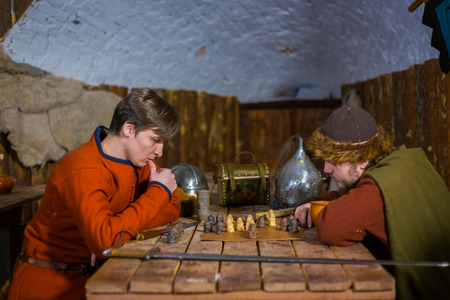 Two men in russian ethnic suit playing medieval popular strategy board game - tafl. Folk,...