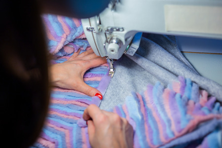 Close up shot - professional tailor, fashion designer sewing colorful fur coat with sewing machine...