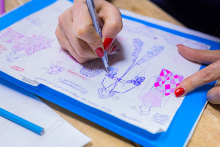 Close up shot - hands of professional tailor, designer drawing fashion sketch at atelier, studio. Dressmaking, creativity and tailoring conceptの写真素材