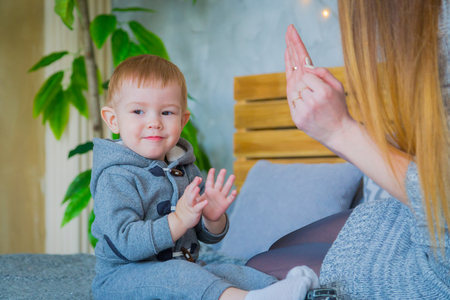 Young mother and her baby son playing togerher on the bed at homeの写真素材