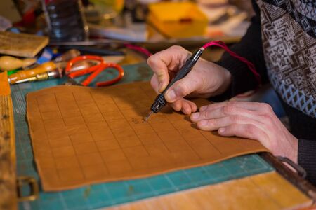 Professional male skinner, tanner making decorative details on leather playing field for strategy...