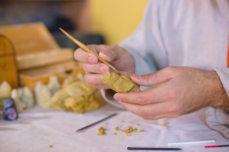 Professional male potter in russian ethnic shirt making clay figure for medieval popular strategy board game - tafl. Handwork, crafting and traditional arts conceptの写真素材