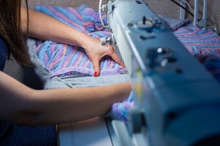 Close up shot - professional tailor, fashion designer sewing colorful fur coat with sewing machine...