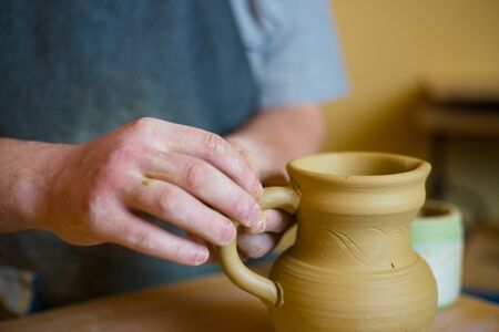 Professional male potter working in workshop, studio - putting handle on ceramic jar. Handmade, small business, crafting work conceptの写真素材