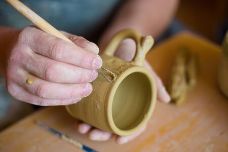 Professional potter making pattern on clay mug with special tool in pottery workshop, studio. Crafting, artwork and handmade conceptの写真素材