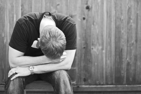 blond man sitting alone with his head downの写真素材
