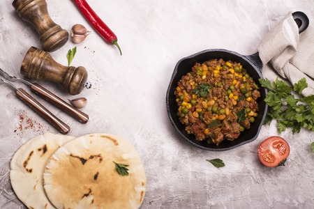 Spicy chili con carne with kidney bean and ground beef and ingredients over stone table. Top view
