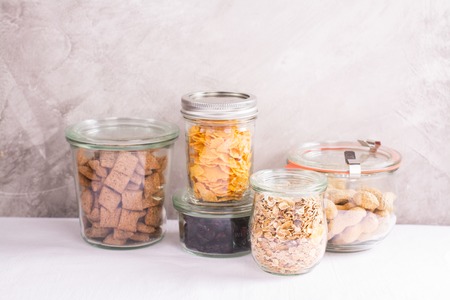 Assortment of cereals, flakes, nuts and berries in storage glass jars over kitchen table. Homemade granola bar ingredientsの写真素材