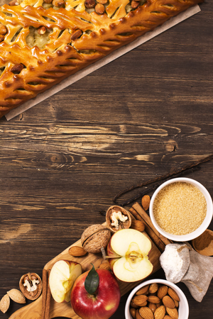 Apple pie with almonds and cinnamon and ingredients over brown wooden tableの写真素材