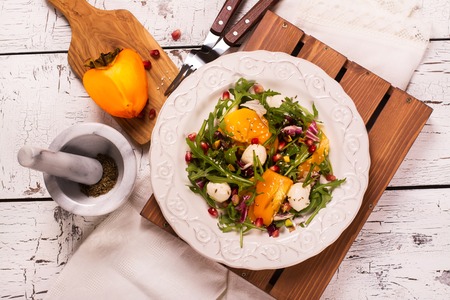 Fresh colorful summer salad with persimmon, arugula, mozzarella  cheese and pomegranate seeds. Top view. Selective focusの写真素材