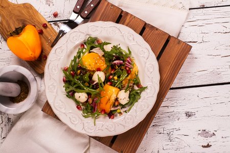 Fresh colorful summer salad with persimmon, arugula, mozzarella  cheese and pomegranate seeds. Top view. Selective focusの写真素材
