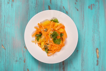 Salad with fresh carrot, orange slices, pumpkin and  sunflower seeds over blue wooden table. Top viewの写真素材