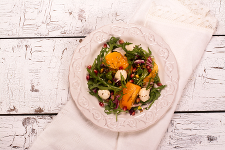 Fresh colorful summer salad with persimmon, arugula, mozzarella  cheese and pomegranate seeds. Top view. Selective focusの写真素材