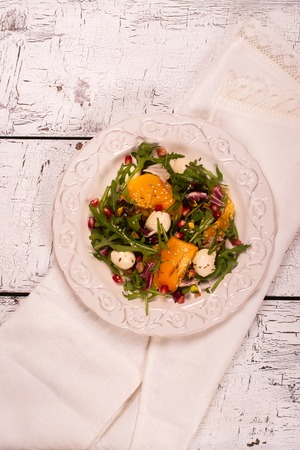 Fresh colorful summer salad with persimmon, arugula, mozzarella  cheese and pomegranate seeds. Top view. Selective focusの写真素材