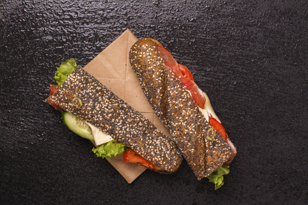 Tasty rye bread sandwiches with ham, cheese and vegetables over black stone tableの写真素材