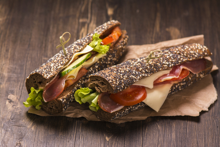 Two healthy sandwiches with ham, cheese and vegetables over grunge wooden tableの写真素材