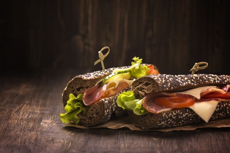 Two healthy sandwiches with ham, cheese and vegetables over grunge wooden tableの写真素材