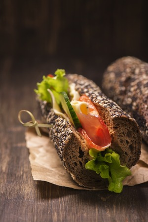 Tasty rye bread sandwhiches with ham, cheese and vegetables over dark wooden tableの写真素材
