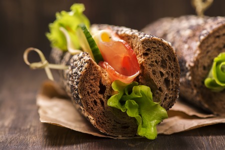 Tasty rye bread sandwhiches with ham, cheese and vegetables over dark wooden tableの写真素材