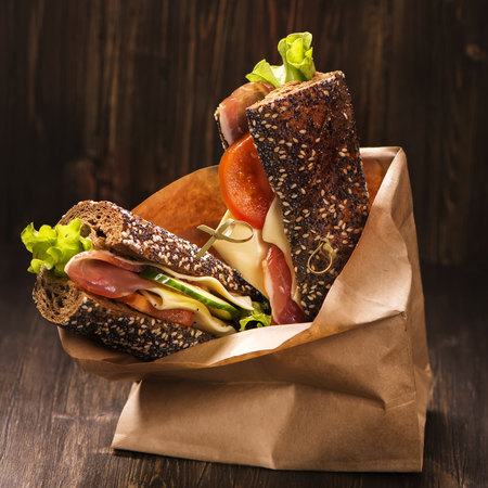 Rye bread sandwiches with ham, cheese and vegetables in a craft paper bag. Take away food. Selective focusの写真素材