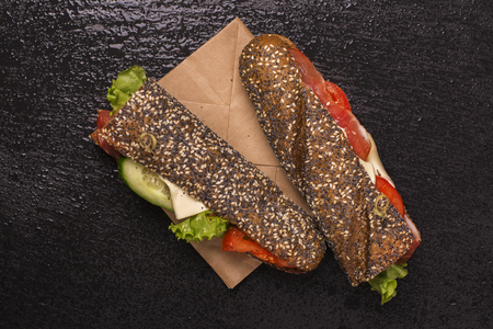 Tasty rye bread sandwiches with ham, cheese and vegetables over black stone tableの写真素材