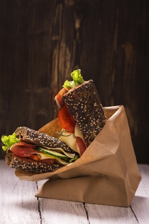 Rye bread sandwiches with ham, cheese and vegetables in a craft paper bag. Take away food. Selective focusの写真素材