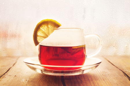 Black tea with lemon slices in a glass cup. View over wet rainy window. Toned image. Selective focusの写真素材
