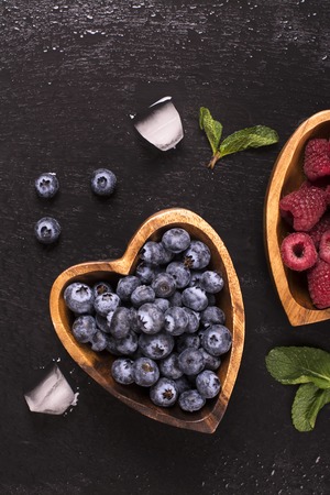 Blueberry and raspberry in heart shaped wooden bowls over black stone background. Top viewの写真素材