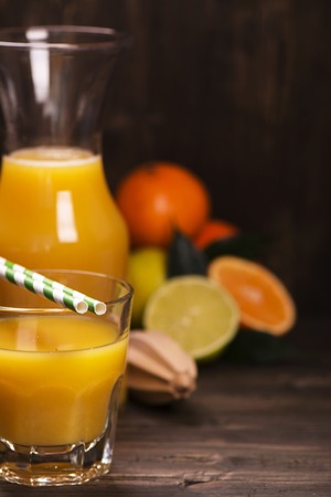 Glass of fresh homemade orange juice with pile of fruits over grunge wooden tableの写真素材