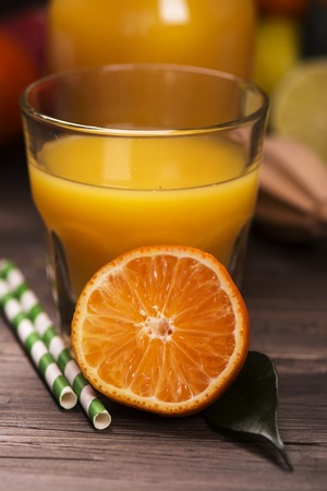 Glass of fresh homemade orange juice with pile of fruits over grunge wooden tableの写真素材