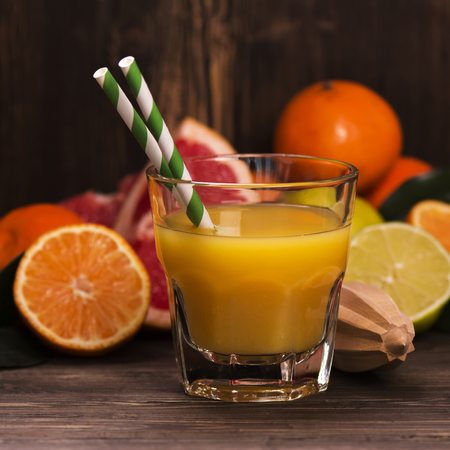 Glass of fresh homemade orange juice with pile of fruits over grunge wooden tableの写真素材