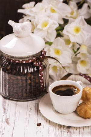 Coffee beans in vintage jar, cup of black coffee and pastry over white wooden tableの写真素材