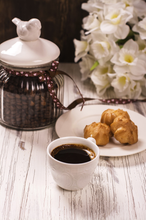 Coffee beans in vintage jar, cup of black coffee and pastry over white wooden tableの写真素材