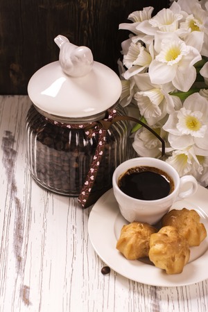 Coffee beans in vintage jar, cup of black coffee and pastry over white wooden tableの写真素材
