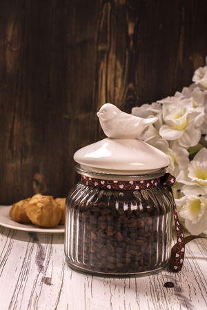 Coffee beans in vintage jar, cup of black coffee and pastry over white wooden tableの写真素材