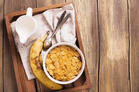 Tasty and healthy breakfast on wooden tray. Female hand holding jar and adding milk into the bowl. Top view.の写真素材