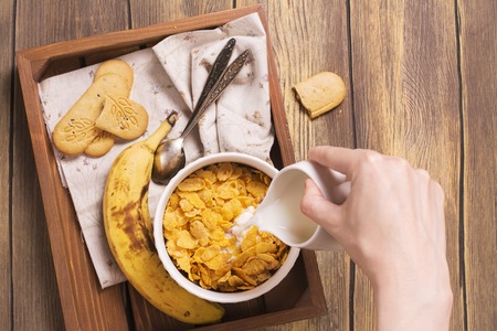 Tasty and healthy breakfast on wooden tray. Female hand holding jar and adding milk into the bowl. Top view.の写真素材