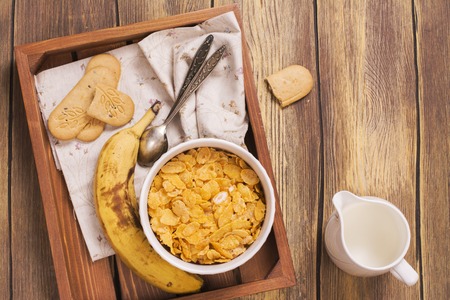 Tasty and healthy breakfast on wooden tray. Female hand holding jar and adding milk into the bowl. Top view.の写真素材