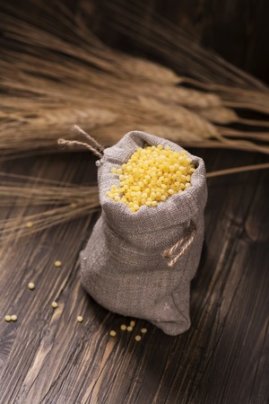 Golden pearl couscous in a burlap bag and spikelets over grunge wooden table. Vintage styleの写真素材