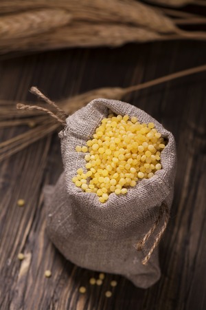 Golden pearl couscous in a burlap bag and spikelets over grunge wooden table. Vintage styleの写真素材