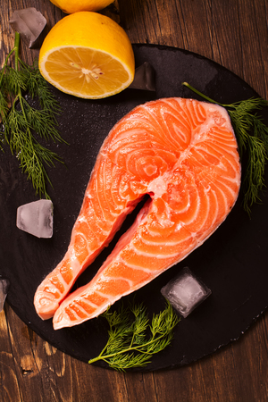 Raw salmon steak with lemon and herbs over wooden background. Healthy food conceptの写真素材